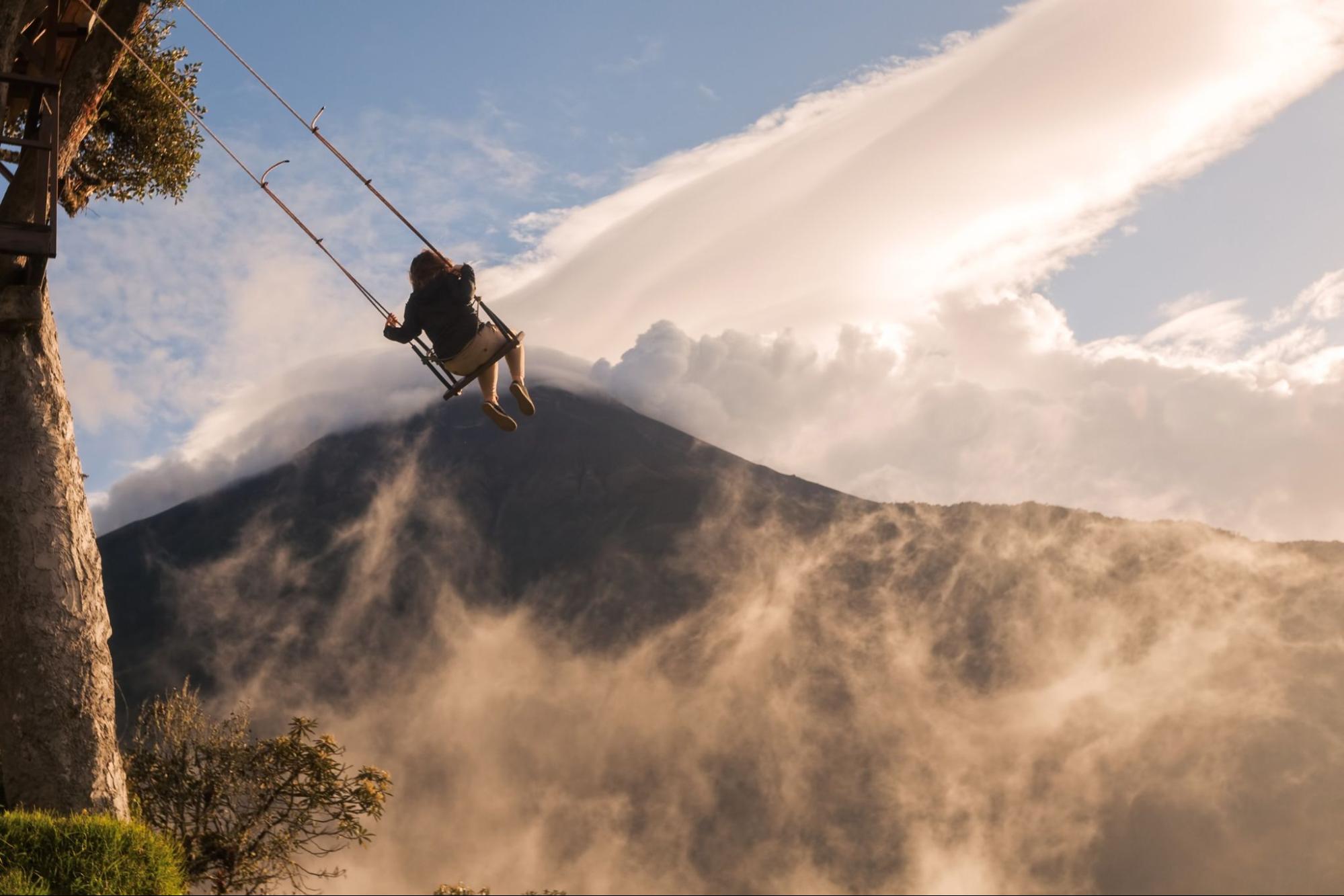Unidentified Silhouette Of A Happy Tourist Girl Swinging On A Swing Above The Andes Mountains, Tungurahua Volcano In Background